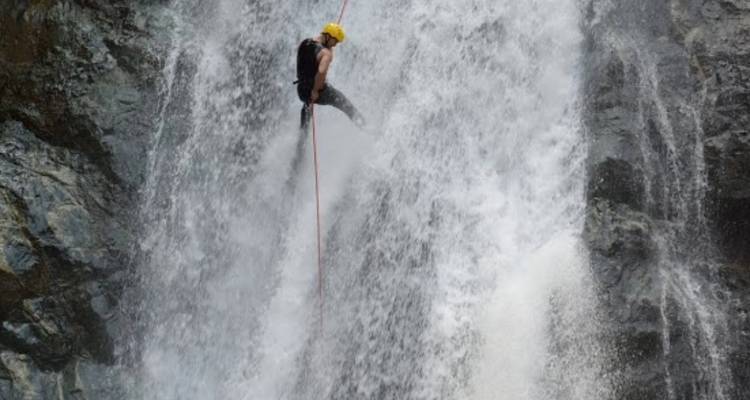 Aventurero con casco desciende en rappel por la cara de una cascada rugiente.