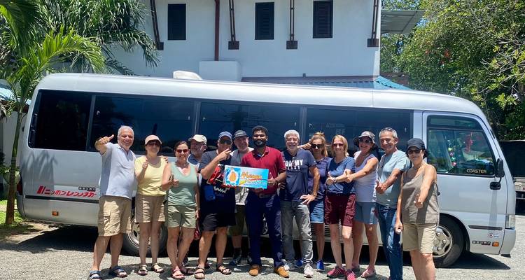 Group of tourists posing in front of a van in a tropical setting.