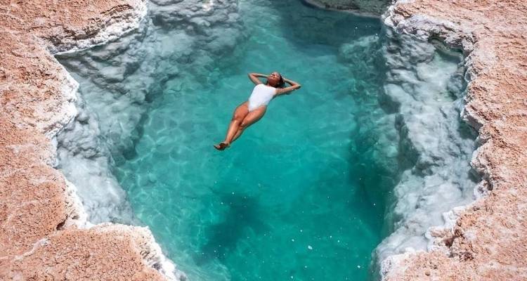 Persoon drijvend in een helder turquoise zwembad in een woestijnlandschap.