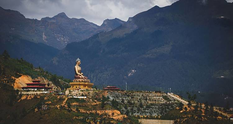 Große sitzende Buddha-Statue auf einem Hügel mit bergiger Landschaft im Hintergrund.