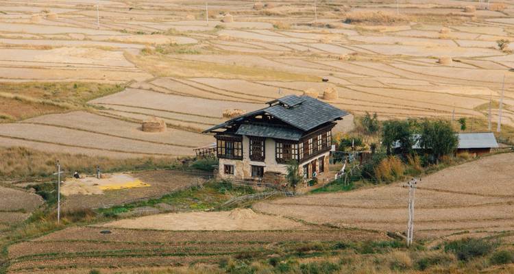 Traditionelles bhutanesisches Haus in einer ländlichen Landschaft mit Feldern.