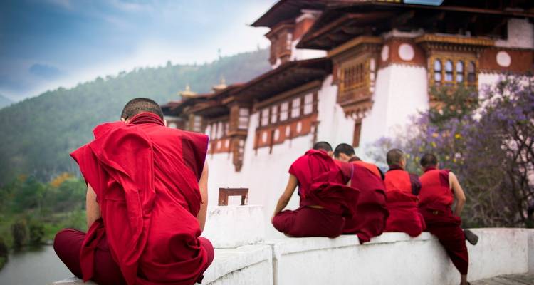 Mönche in roten Roben, die in der Nähe eines traditionellen bhutanischen Gebäudes sitzen.