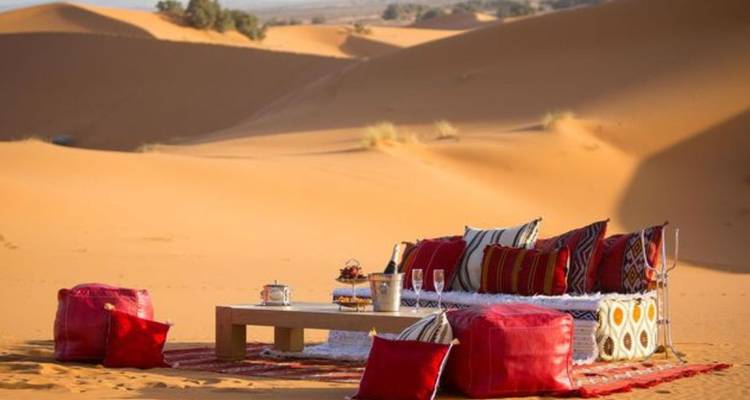 Lage tafel met kleurrijke kussens en traditionele theeset gerangschikt op het open woestijnzand.