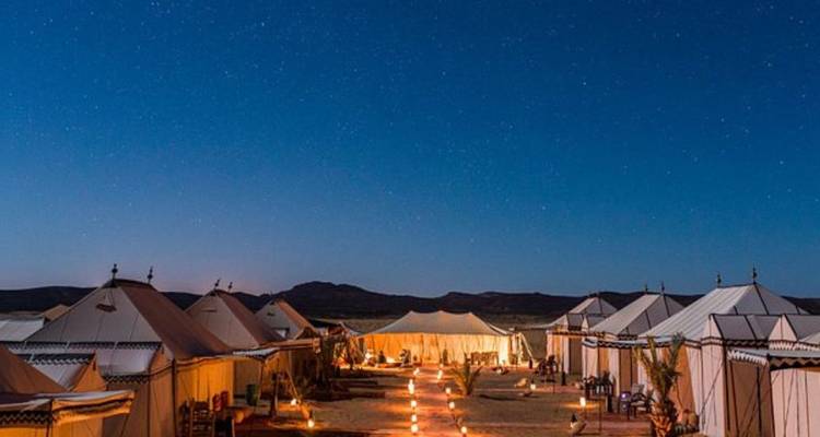 Rij verlichte woestijntenten onder een sterrenhemel in een uitgestrekte zandvlakte.