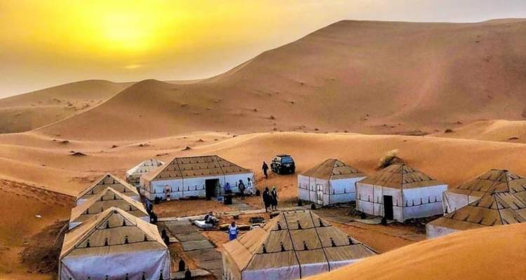 Groep witte canvastenten die een woestijnkamp vormen, omlijst door hoge duinen bij zonsopgang.