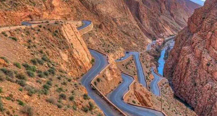 Kronkelende haarspeldbochtenweg snijdt door steile roodachtige kanjoonwanden met een rivier ver beneden.