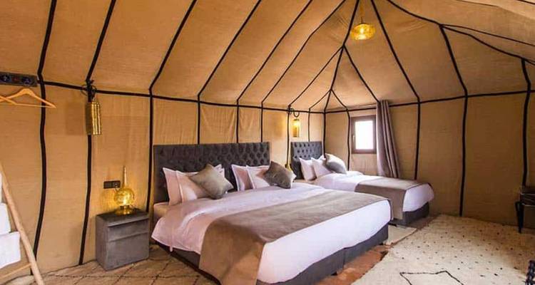 Ruime luxe tent interieur met twee tweepersoonsbedden, zachte verlichting en aardse decoratie.