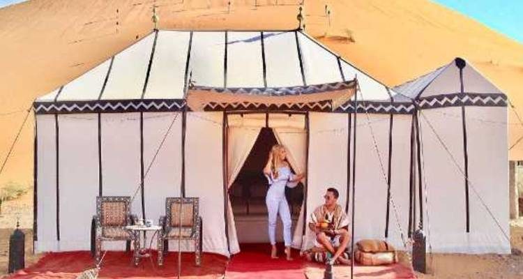 Stel dat ontspant buiten een witte canvas woestijntent met hoge zandduinen op de achtergrond.