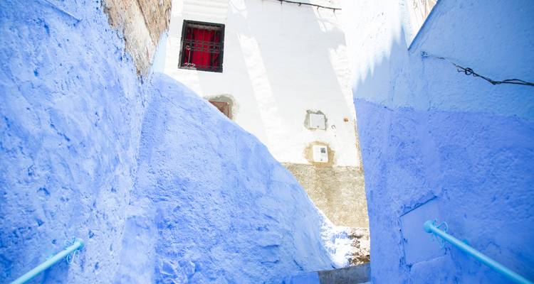 Ruelle peinte en bleu vif avec des murs blanchis à la chaux et des escaliers étroits dans une ville de montagne marocaine.