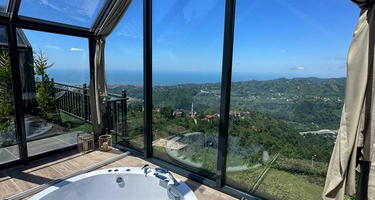 Uitzicht vanuit een met glas omsloten ruimte met heuvels en zee in de verte.