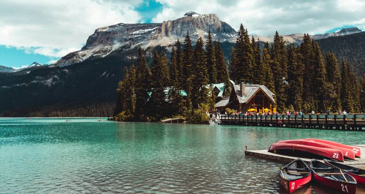 Rustig meer met kano's en een houten lodge, omgeven door beboste bergen.