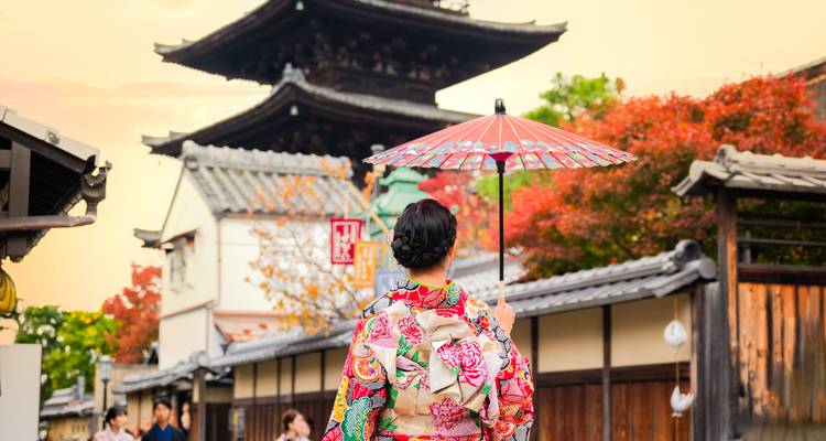Une femme en vêtements traditionnels colorés tenant un parapluie devant des pagodes.