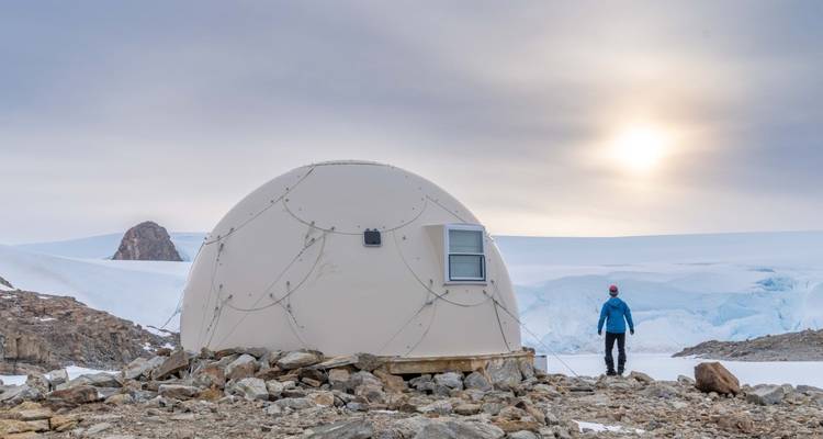 Personne debout à côté d'une structure en dôme sur un terrain rocheux.