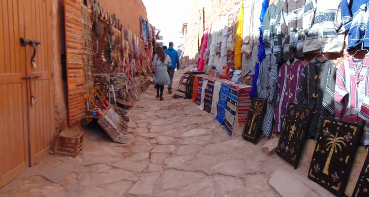Mercado en calle estrecha con alfombras y textiles coloridos en exhibición.