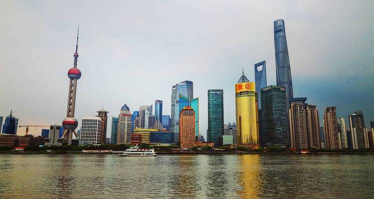 Moderne Skyline von Shanghai mit dem ikonischen Oriental Pearl Tower und Wolkenkratzern, die sich über den Huangpu-Fluss erheben, mit einer Fähre im Vordergrund.