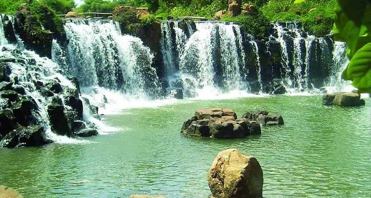 A lush waterfall flowing into a natural pool surrounded by rocks.
