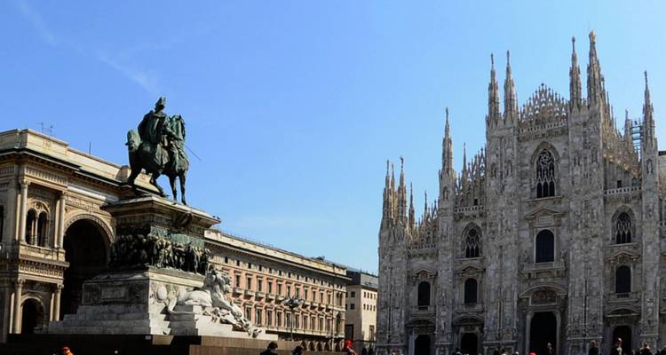 Gran Piazza del Duomo con la fachada ornamentada de la Catedral de Milán y una estatua ecuestre bajo un cielo azul despejado.
