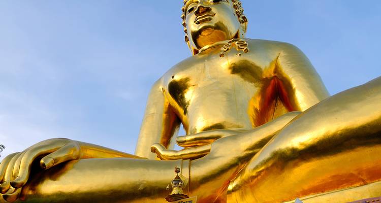 Primer plano de una reluciente estatua dorada de Buda sentado contra un cielo azul despejado.