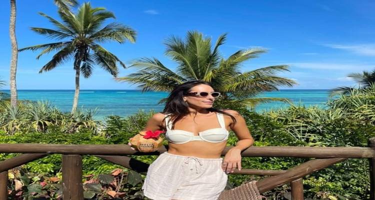 Woman posing by a beach with palm trees and turquoise water.