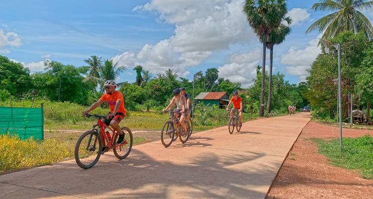 Les cyclistes pédalent le long d'un sentier rural pavé bordé de verdure tropicale et de ciel bleu éclatant.