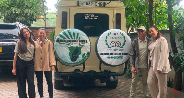 Vier Reisende posieren neben einem Safariajeep mit der Marke Africa Natural Tours in einem mit Laub geschmückten Innenhof.