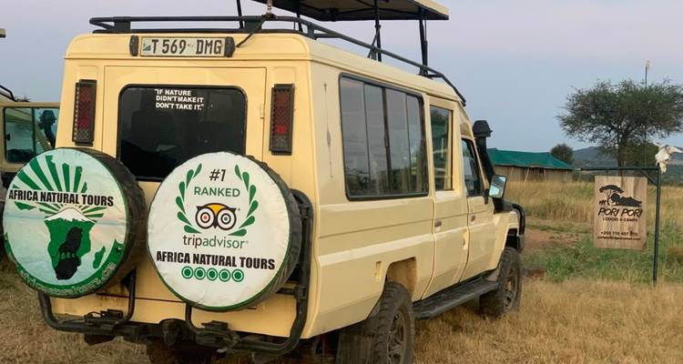 Geparkter Safari-Jeep an einem rustikalen Buschcampingplatz mit nahegelegenen Zelten aus Segeltuch.