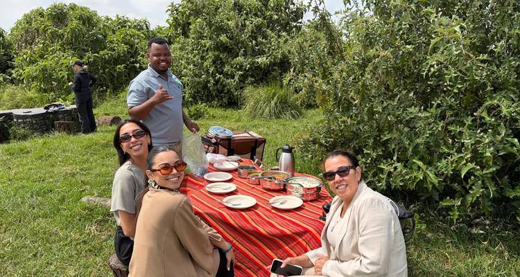 Reisende genießen ein Picknick im Freien auf einem rot gestreiften Tuch inmitten üppiger Vegetation auf einer Safari.