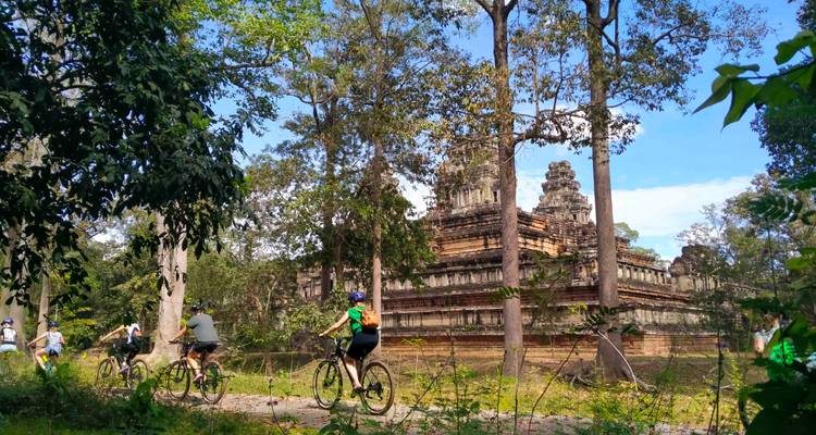 Los ciclistas pasan por un templo de piedra escalonado en lo profundo de la selva camboyana con un cielo azul despejado arriba.