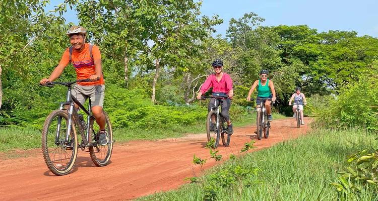 Los ciclistas avanzan en fila india por un camino de tierra roja a través del exuberante paisaje rural camboyano
