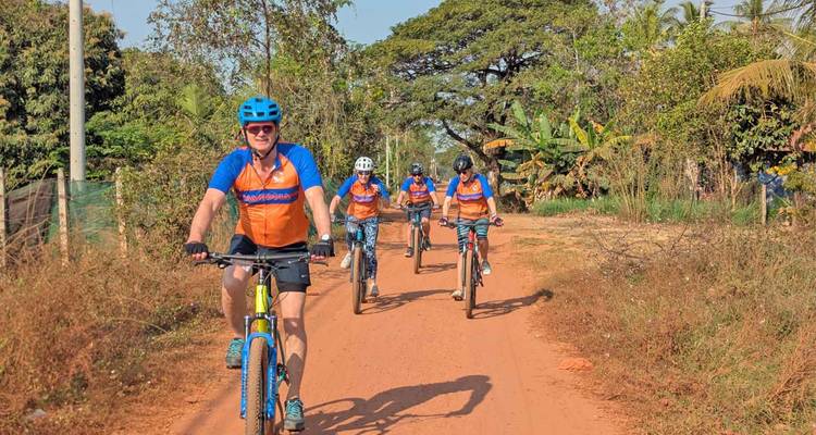 Grupo de ciclistas con uniforme a juego pedaleando en un camino rural polvoriento
