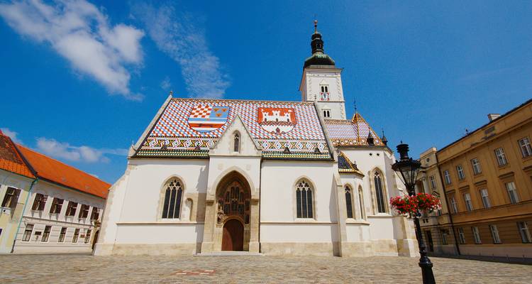 St. Mark's Church in Zagreb with its colorful tiled roof stands bright against a clear blue sky.