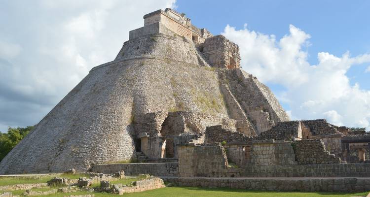 Pyramide maya avec des ruines sous un ciel partiellement nuageux.