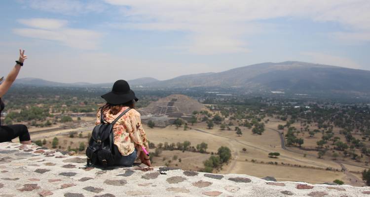 Reisende sitzen auf antiken Steinen mit Blick auf die Pyramide des Mondes in Teotihuacán mit Panoramablick auf das Tal.