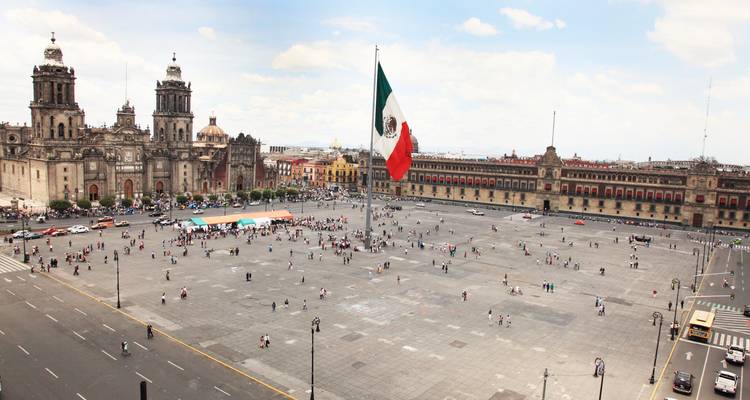 Luftaufnahme des riesigen Zócalo-Platzes von Mexiko-Stadt mit der mexikanischen Flagge, der Metropolitankathedrale und dem Nationalpalast, umgeben von geschäftigen Menschenmassen.