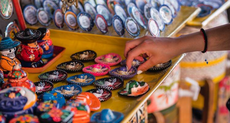 Nahaufnahme einer Hand, die lebendige mexikanische Souvenirmagnete und Figuren an einem Marktstand auswählt.