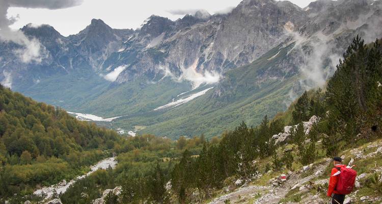 Randonneur marchant dans une vaste vallée entourée de montagnes imposantes.