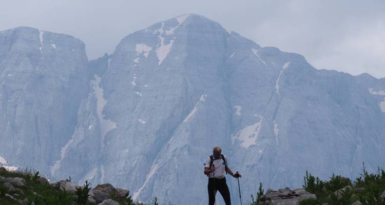 Hiker standing in front of massive mountains, foggy weather.