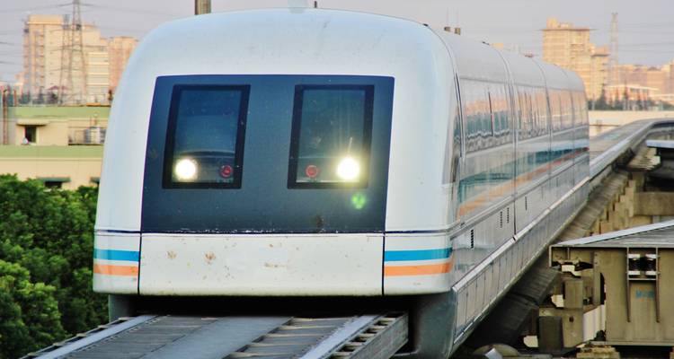 Tren de levitación magnética de alta velocidad aproximándose en una vía elevada con la ciudad de fondo