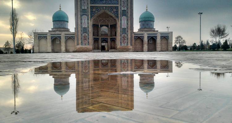 Mosque with reflections on water with domes and intricate tile work.