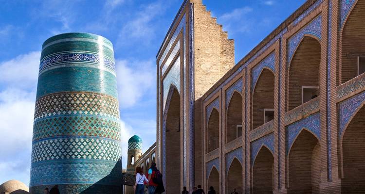 Minaret and mosque with decorative tiles, people walking.