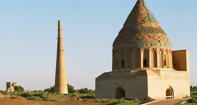 Ancient mausoleum and minaret in a desert landscape.