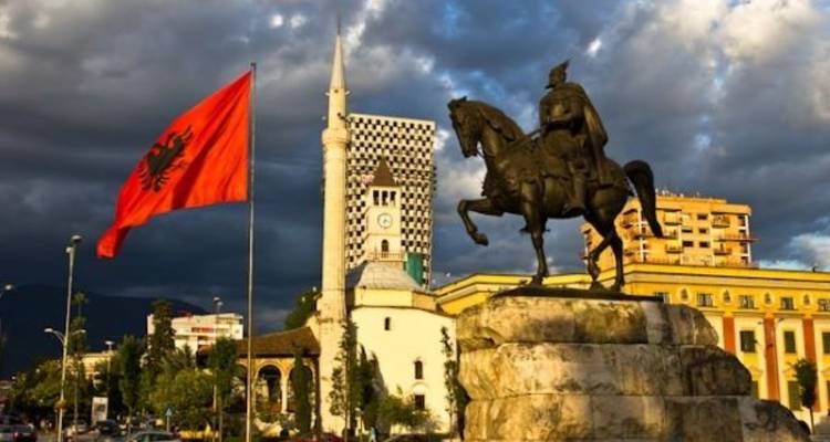 Statue with an Albanian flag and mosque in the background.