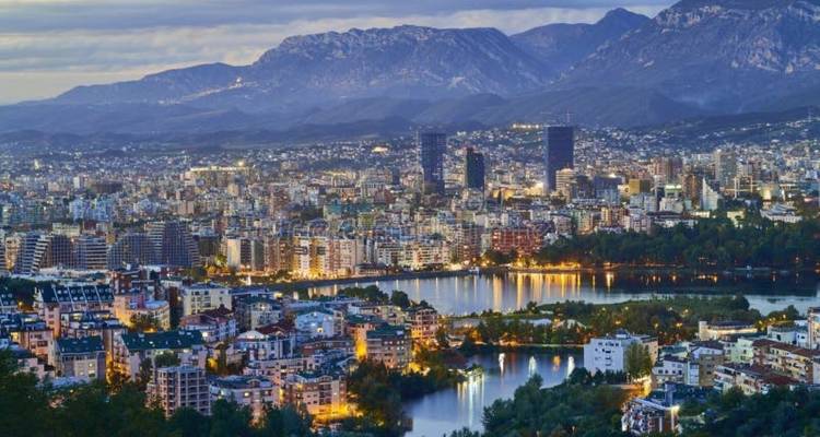 Panoramic view of a city at dusk surrounded by mountains.