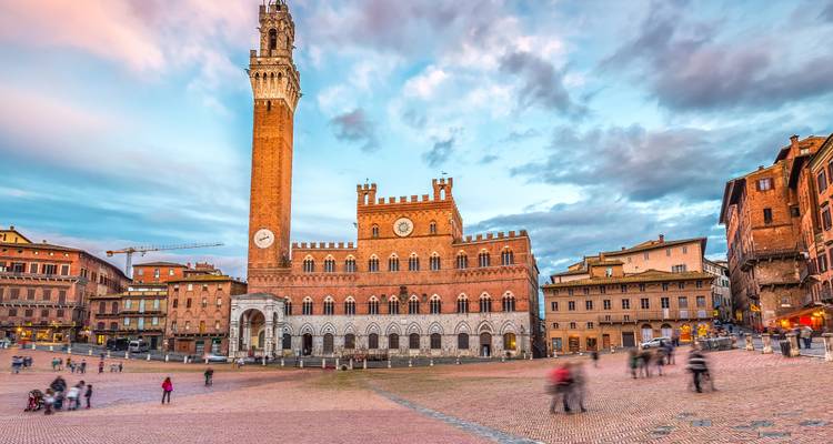 Twilight scene of Siena’s Piazza del Campo with the Palazzo Pubblico and Torre del Mangia, blurred visitors crossing the square.