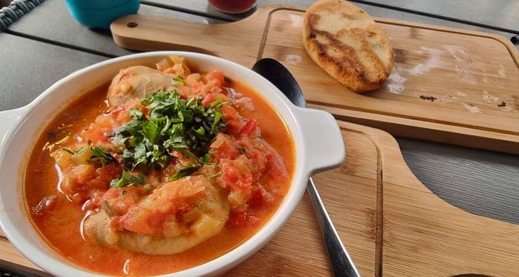 Plato de jjárjinais georgianos en una salsa de tomate y hierbas aromáticas, acompañados de pan fresco en una tabla de madera.