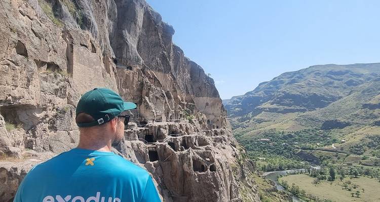 El viajero observa las viviendas en cuevas del acantilado de Vardzia con un valle fluvial extendiéndose más allá.