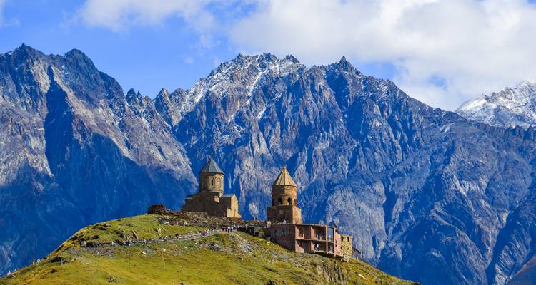 La Iglesia de la Trinidad de Gergeti encaramada en una cresta verde bajo los imponentes picos rocosos del Cáucaso.