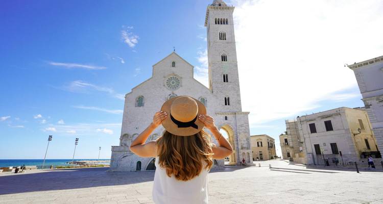 Jonge vrouw met hoed kijkend naar de kathedraal van Trani en het heldere plein aan zee op een zonnige dag.