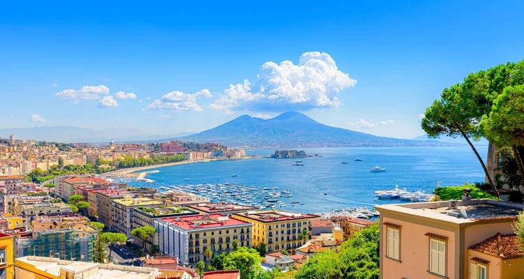 Panoramablick auf eine Küstenstadt mit einem Vulkan im Hintergrund.