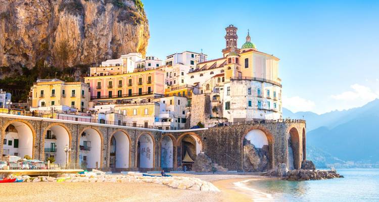 Colorful cliffside village of Atrani on the Amalfi Coast with arched sea wall and sandy beach.